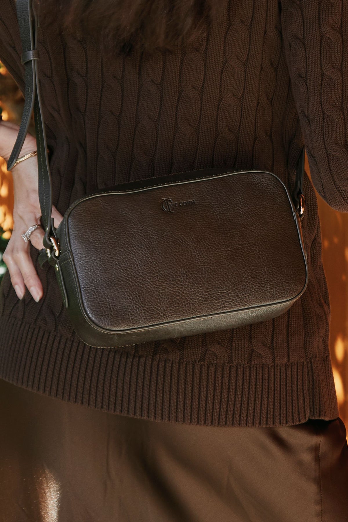 Grey leather crossbody bag held by a person wearing a brown sweater.