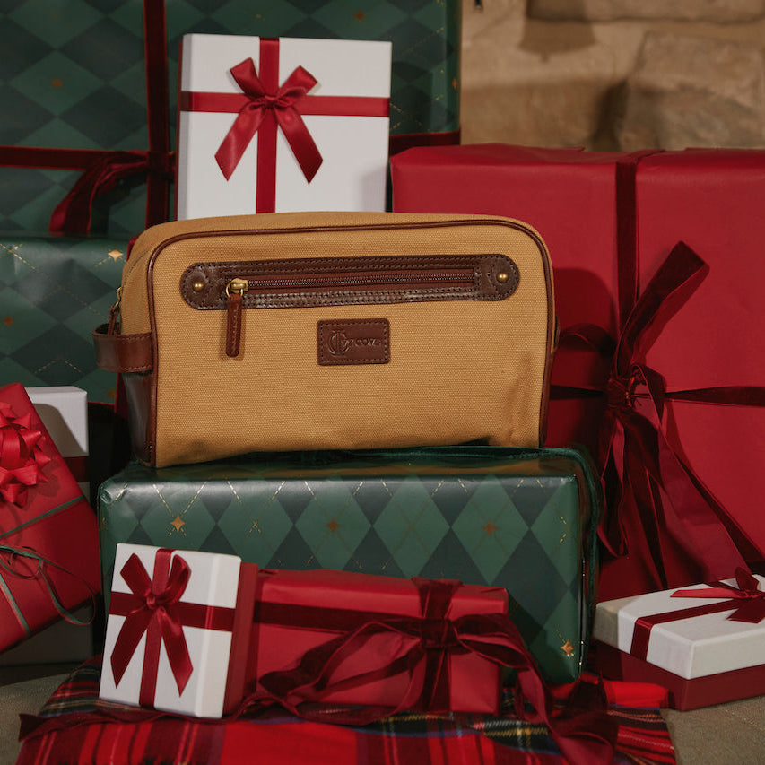 Brown canvas dopp kit on a pile of Christmas presents with red and green wrapping.