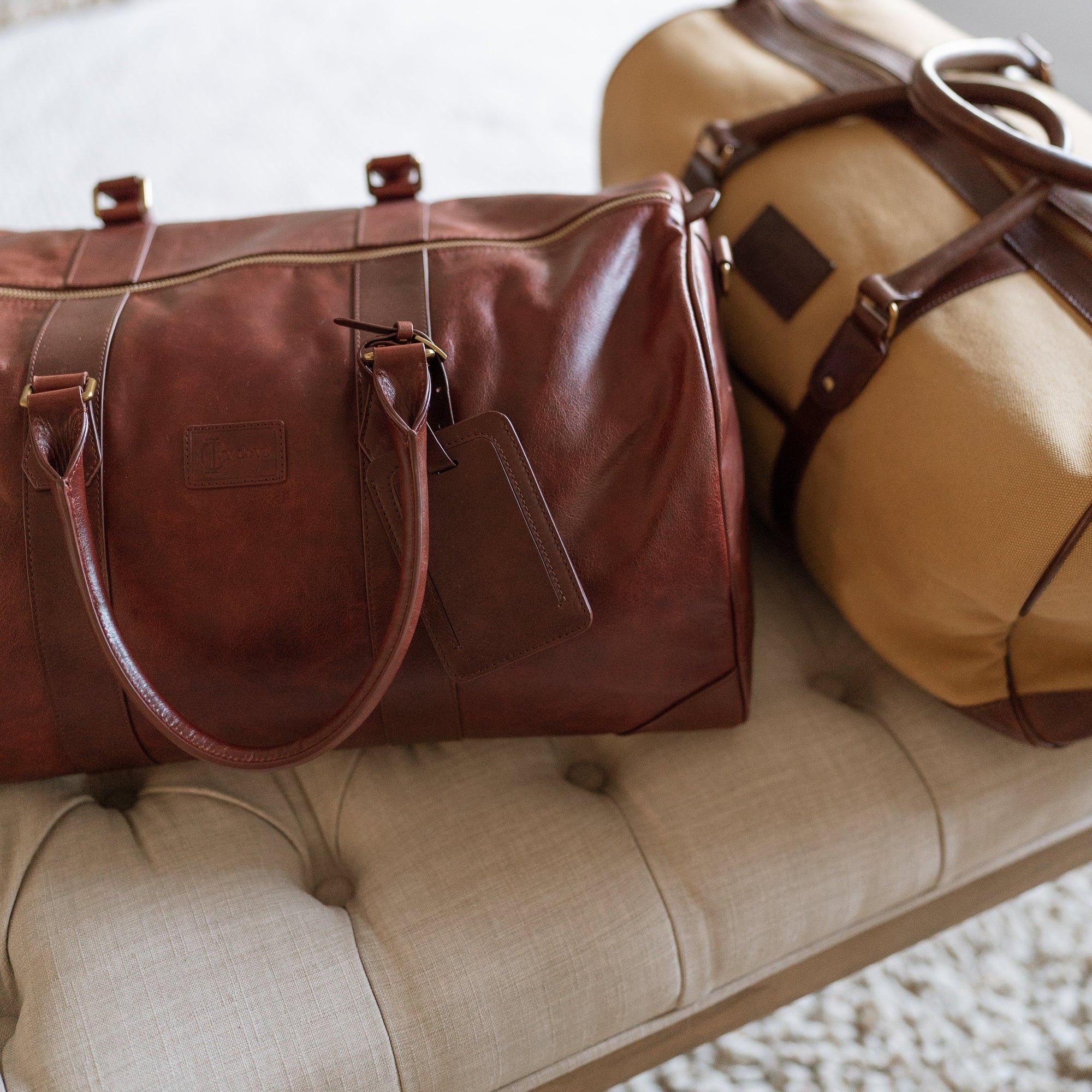 Two brown leather duffel bags on a beige surface