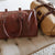 Two brown leather duffel bags on a beige surface