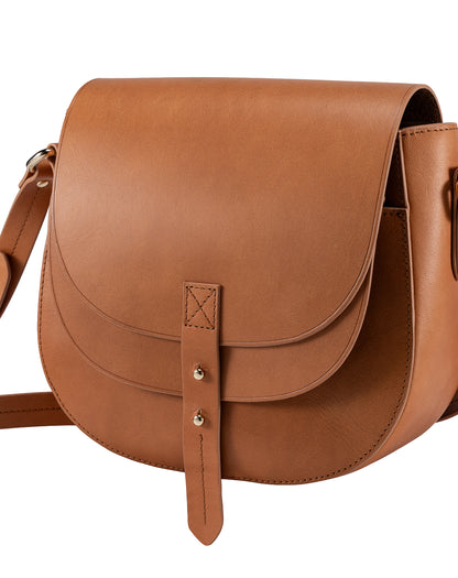 Saddle leather crossbody bag with curved flap and leather tab closure, three-quarter view