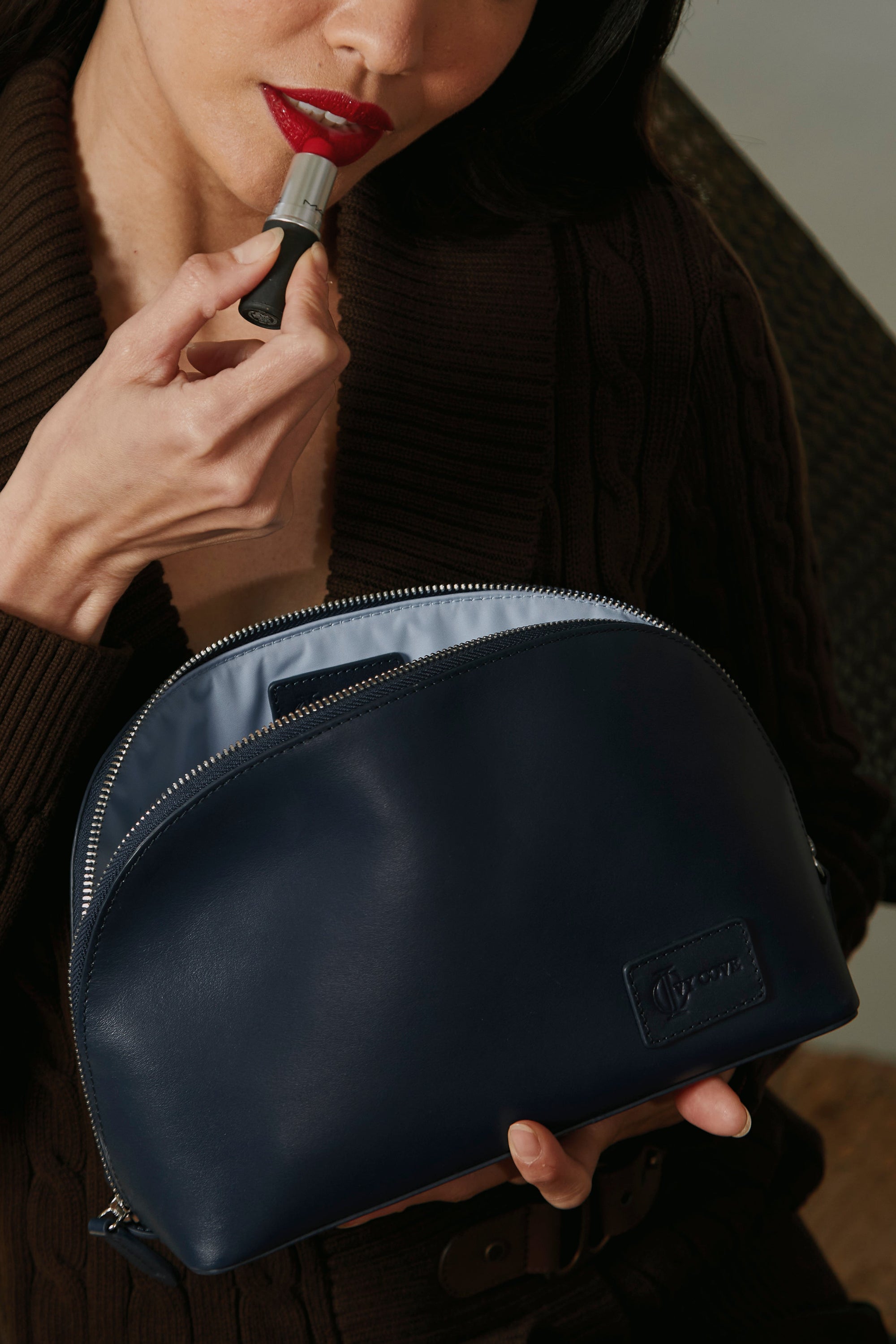Woman applying lipstick with a blue makeup bag in the foreground