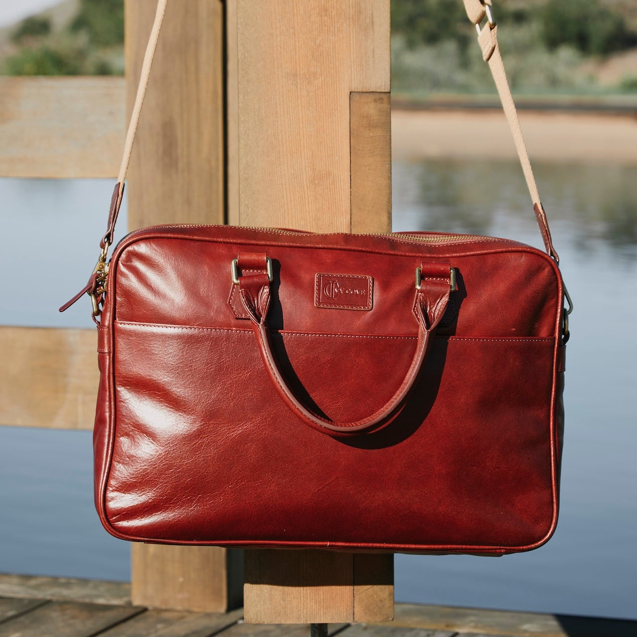 Red leather briefcase with a strap on a wooden post by a body of water