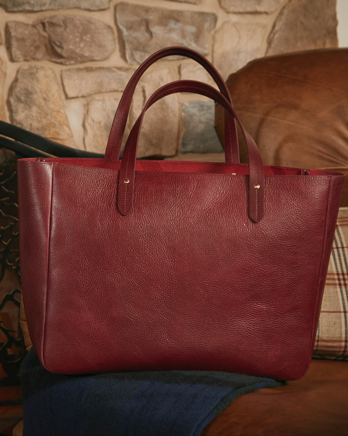 Red leather tote bag on a brown couch with a stone fireplace in the background