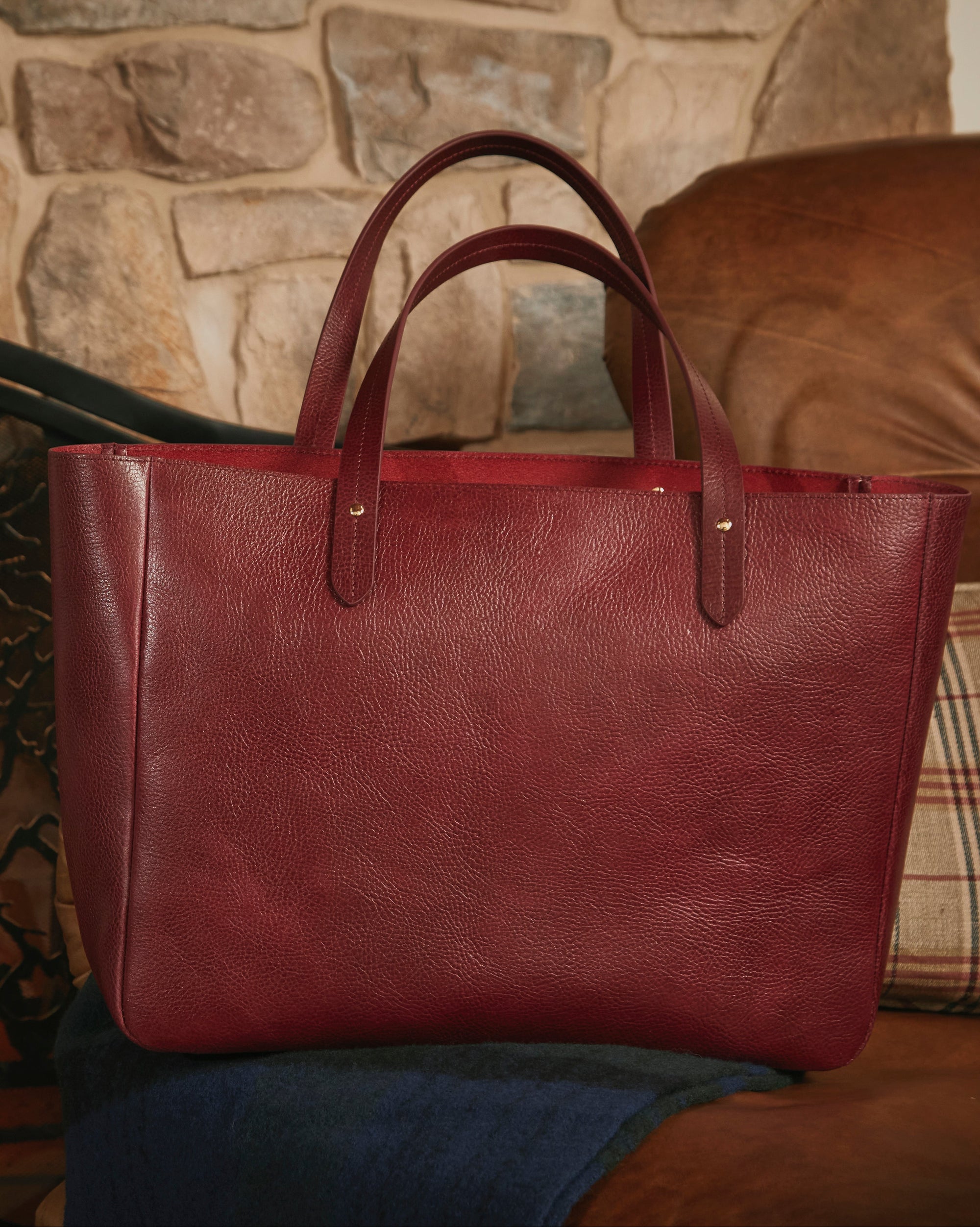 Red leather tote bag on a brown couch with a stone fireplace in the background