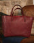 Red leather tote bag on a brown couch with a stone fireplace in the background