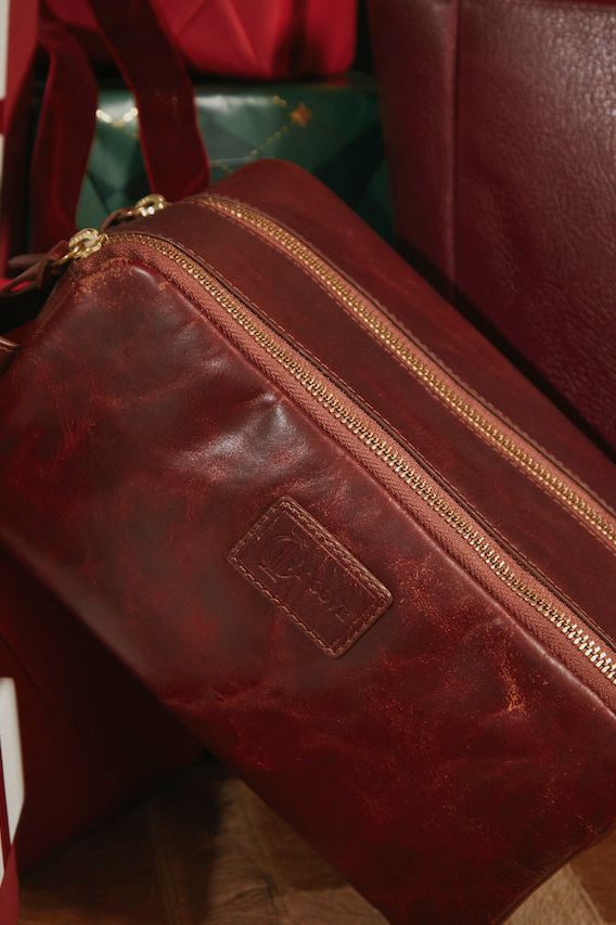 Brown leather bag with gold zipper on a surface with gift boxes and a black pouch.