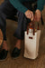 Person holding a bottle of wine in a beige tote bag on a textured surface